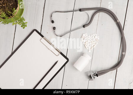 Medizinisches Konzept - Stethoskop, pad, Flasche und weißen Herzen von Pillen und Kapseln auf weißem Schreibtisch aus Holz Stockfoto