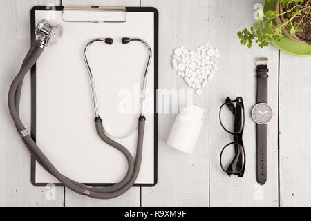 Medizinisches Konzept - Stethoskop, pad, Glas, Uhren, Flaschen- und weißen Herzen von Pillen und Kapseln auf weißem Schreibtisch aus Holz Stockfoto