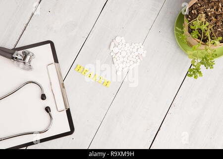 Medizinisches Konzept - Stethoskop, pad, weißes Herz von Pillen und Kapseln, Gesundheit Beschriftung auf weißem Schreibtisch aus Holz Stockfoto