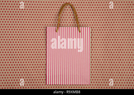 Celebratory Konzept - Handgemachte gestreifte Shopping Bag, Geschenkbeutel für das Handwerk Papier Hintergrund in Rot Polka Dots Stockfoto