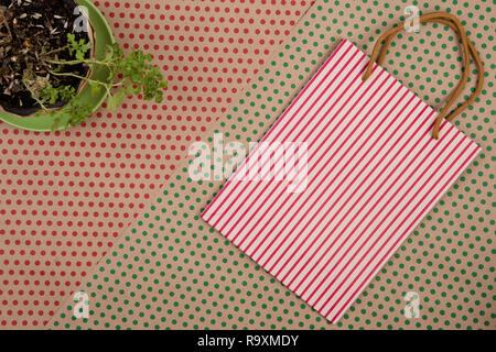 Celebratory Konzept - Handgemachte gestreifte Shopping Bag, Geschenkbeutel und Blume auf Handwerk Papier Hintergrund in Rot und Grün Polka Dots Stockfoto