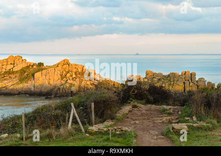 Weg zum Felsen mit Mont Saint Michel in der Ferne, Felsen, die von Sonnenstrahlen beleuchtet kurz vor Sonnenuntergang, Bretagne, Frankreich Stockfoto