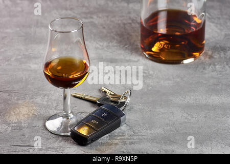 Glas und Flasche Whiskey auf einem steinernen Tisch und Autoschlüssel. Fahren in der Betrunkenheit Stockfoto