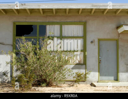 Eine überwachsene Bush verschleiert ein defektes Fenster an den Dünen, einem verlassenen Motel/Apartmentanlage an der historischen Route 66 in der Nähe von Barstow, Kalifornien. Stockfoto