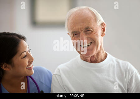 Lächelnde junge Krankenschwester Lachen mit einen älteren Patienten. Stockfoto