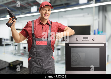 Männliche Arbeiter mit einer Bohrmaschine neben einem elektrischen Ofen in einer Fabrik stehen Stockfoto