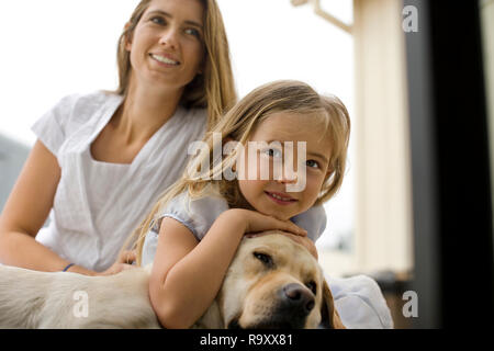 Kleines Mädchen und ihr Lächeln Mutter auf dem Boden mit ihren Sleepy Dog entspannen. Stockfoto