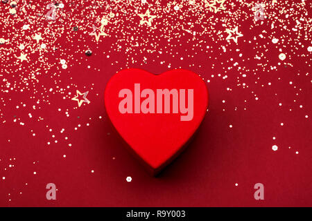 Herzförmige Box mit goldenen Glitter und Konfetti auf rot festlich Hintergrund. Valentine's Holiday Konzept. Ansicht von oben. Stockfoto