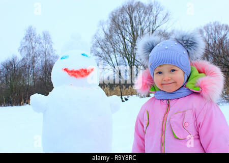 Portrait of smiling baby in lustigen Mütze mit zwei komische Ohren. Kleines Mädchen und Schneemann Kopf. Kleine Mädchen gemacht Schneemann. Winter Spaß Kinder Stockfoto