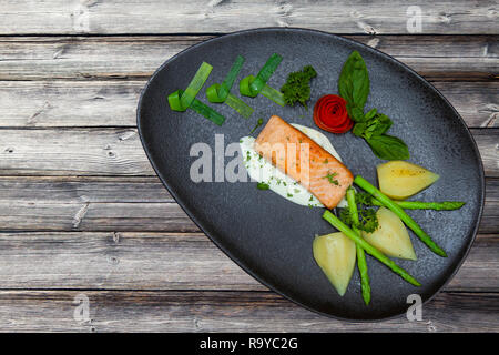 Atlantischer Lachs mit Rucola, mit Gemüse auf einer schwarzen Platte eingerichtet, alte Holz Muster Wand Hintergrund. Stockfoto