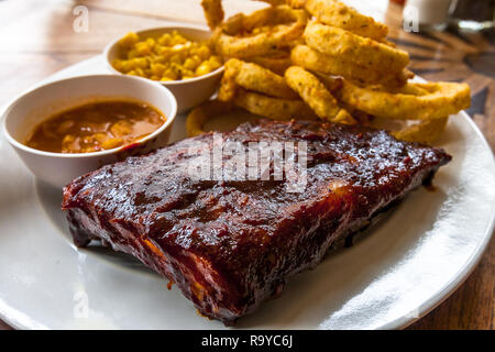 Smoked BBQ Ribs auf einem weißen Teller mit Zwiebelringen und Mais. Stockfoto