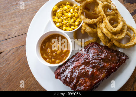 BBQ Ribs, gebackene Bohnen, Zwiebeln auf einem weißen Teller serviert. Stockfoto