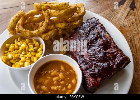 Eine große weiße Platte voller BBQ Ribs mit Mais und Bohnen. Stockfoto