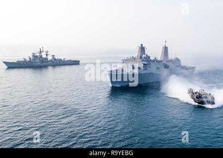 Ein U.S. Navy Landing Craft, Luftpolster Manöver von der U.S. Navy San Antonio-Klasse amphibious Transport dock Schiff USS Anchorage zusammen Segeln mit der indischen Marine Zerstörer ins Rajput, Links, während kooperative Übungen zum 26. Dezember 2018 im Indischen Ozean. Stockfoto