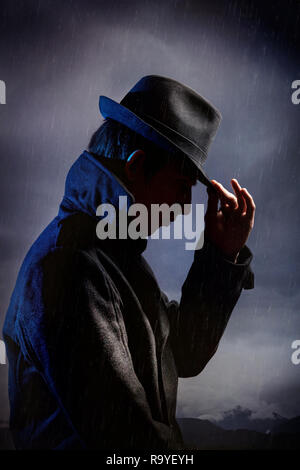 Mann in schwarzen Hut im Regen an der Dunkelheit bedeckten Himmel Stockfoto