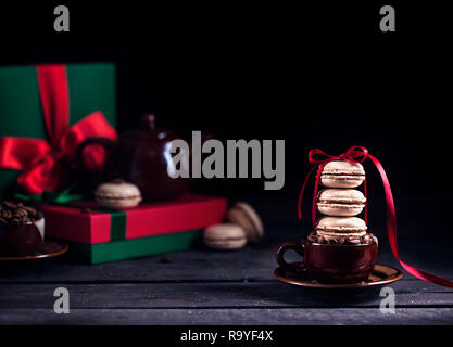 Braun macarons in Tasse mit Kaffee in der Nähe des heutigen Weihnachten Boxen auf schwarzen Hintergrund mit Kopie Raum Stockfoto