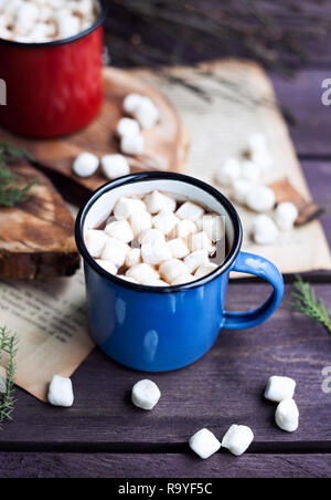 Kakao mit Marshmallows in Blau und Rot Becher auf Holztisch im Winter Stockfoto