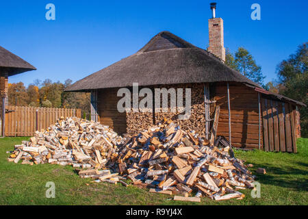 Stapel und Wand von birke holz und gestapeltes Rundholz bereit für den Winter, die auf dem Gras in der Nähe eines Litauischen typische Holzhaus Stockfoto