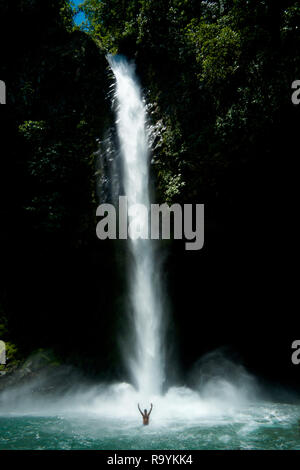 Wasserfall, einen Mann in den Pool an der Unterseite des Wasserfalls mit den Händen in der Luft mit der Größenunterschied zwischen Mann und Stockfoto