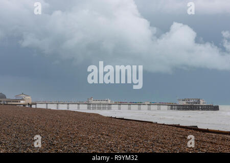 Der schindelige Kieselstrand und der viktorianische Pier in Worthing, West Sussex an einem bewölkt überwölbten Wintertag mit Felsen. Stockfoto