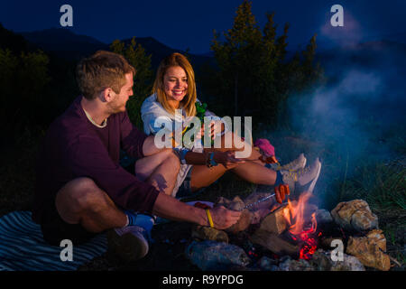 Mann und Frau rosting Würstchen am Lagerfeuer, trinken Bier und ...