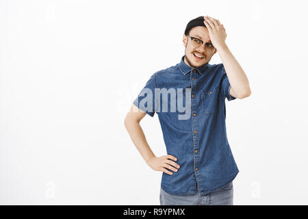 Und junge männliche Unternehmer versuchen, Lösung der Probleme, die Hand auf die Stirn drehen mit gestört und erschöpft Ausdruck stehend mit Arm auf Taille über graue Wand links finden Gestörte Stockfoto