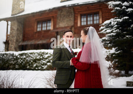 Stilvolle verliebtes Paar am Hochzeitstag niedlich. Braut und Bräutigam zum ersten Mal treffen. Ersten Blick. Winter Hochzeit auf Schneefall mit schönen Holz- Haus c Stockfoto