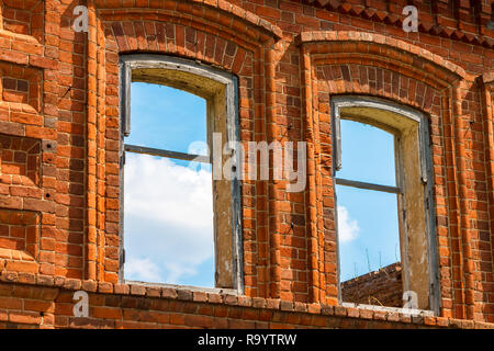 Ein großer ruiniert altes Haus aus rotem Backstein vor einem blauen Himmel mit weißen Wolken. Stockfoto
