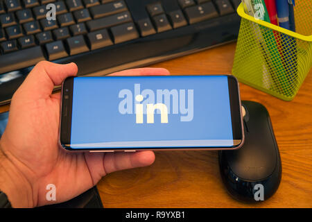 PIATRA Neamt, Rumänien - 30. JULI 2018: Hand hält eine Samsung S8+ Mit Linkedin Logo auf dem Bildschirm angezeigt, Büro Hintergrund. Stockfoto