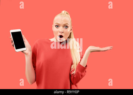 Porträt einer überrascht, lächelnd, glücklich, erstaunt Mädchen mit leerer Bildschirm Mobiltelefon über Coral Hintergrund isoliert. Stockfoto