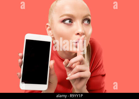 Porträt einer überrascht, lächelnd, glücklich, erstaunt Mädchen mit leerer Bildschirm Mobiltelefon über Coral Hintergrund isoliert. Stockfoto