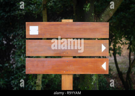 Vorderansicht eines Holzschild mockup mit zwei Signalisierung Pfeile und ein weißes Quadrat. Green forest park Hintergrund. Stockfoto