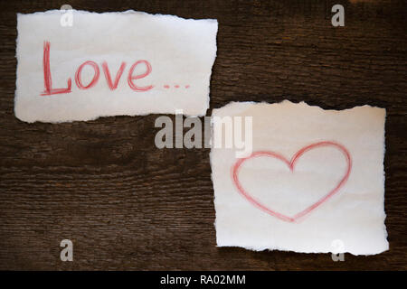 Das Wort Liebe in roten Bleistift auf ein Stück Papier geschrieben ist, das Herz ist rot Bleistift auf ein Blatt Papier gezeichnet. Alles auf einem alten Holz- Board befindet. Stockfoto