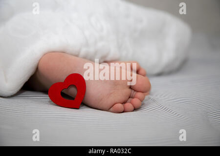 Das Baby schläft unter einer Decke, Füße mit einem roten Herzen für den Urlaub Stockfoto