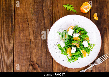 Leckeres Obst und Gemüse Salat. Tangerine, Schafskäse, Rucola und Chia Samen in der Platte. Gesunde Ernährung Konzept. Studio Foto Stockfoto