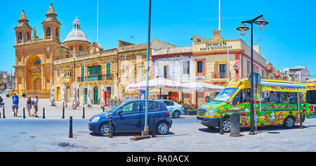 MARSAXLOKK, MALTA - 18. JUNI 2018: Der zentrale Platz des Dorfes mit der Kirche Unserer Lieben Frau von Pomei, touristische Cafés und Eis Auto, zieht Tou Stockfoto