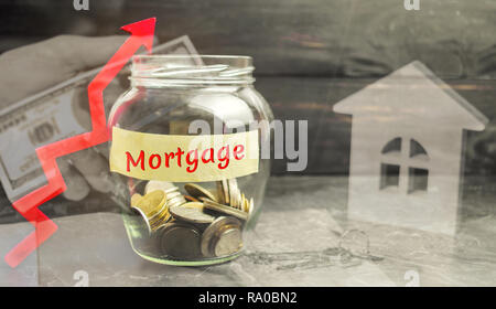 Glas Glas mit Münzen und die Inschrift "Hypothek" und Pfeil nach oben. Die Erhöhung der Zinssätze für Hypotheken. Baufinanzierung und Finanzen. Stockfoto
