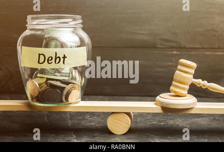 Ein Glas Glas mit Münzen und die Inschrift 'Debt" und "der Richter hammer sind auf der Waage. Konzept der finanziellen Krise und Problemen. Risk Management Stockfoto