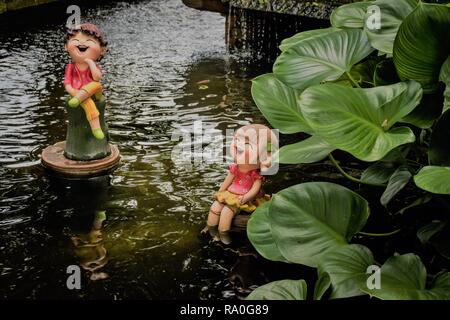 Paar Puppen aus Ton in Teich im kleinen Garten. Tropischen grünen Blätter neben dem Teich Hintergrund. Stockfoto