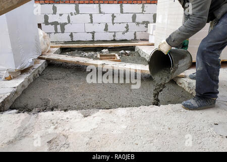 Zusätzliche Arbeiter gießt aus einem Eimer flüssiger Zementmörtel auf dem Boden zwischen den Etagen des Hauses 2018 Stockfoto
