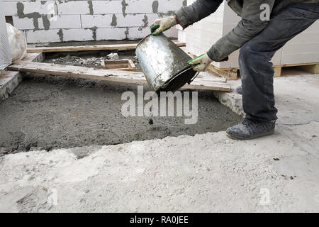 Zusätzliche Arbeiter gießt aus einem Eimer flüssiger Zementmörtel auf dem Boden zwischen den Etagen des Hauses 2018 Stockfoto