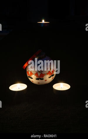 Eine dekorative Weihnachtskugel mit drei Weihnachtsmännern und zwei brennenden Kerzen daneben vor schwarzem Hintergrund - Weihnachtskonzept Stockfoto