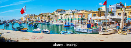 MARSAXLOKK, MALTA - 18. JUNI 2018: Der Hafen von dem Fischerdorf mit vielen kleinen luzzu Boote wird durch traditionelle Häuser der Einheimischen li umgeben Stockfoto