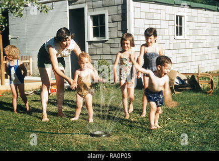 1950s Mutter beobachten Kinder spielen in Sprinkleranlagen, USA Stockfoto