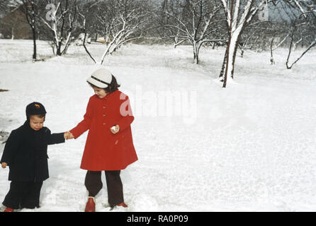 Der 1950er-Jahre ältere Schwester helfen jungen Bruder im Schnee, USA Stockfoto