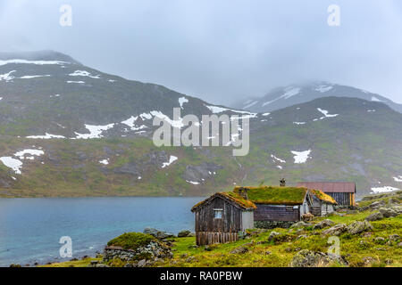 Traditionelle Häuser mit Gras auf dem Dach vor einem See in einem trüben Nebel Tag in Norwegen Stockfoto