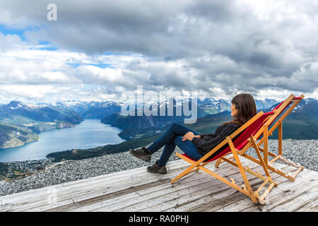 Junge Frau in einem Stuhl in der Spitze der Fjorde mit einem fantastischen Blick in Norwegen sitzen Stockfoto