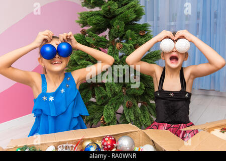 Zwei Mädchen setzen große Weihnachtskugeln zu Ihren Augen Stockfoto