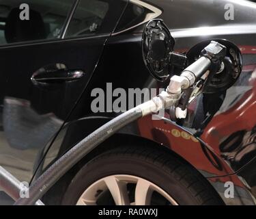 Die Düse in den Gastank öffnen; das Betanken des Fahrzeugs; Kraftstoff an einer Tankstelle in der Nacht. Stockfoto