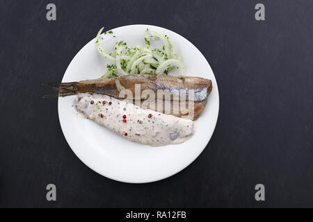 Close up Teil Salzwasser eingelegte Hering Fischfilets mit Zwiebeln und Soße auf weiße Platte über schwarzen Tisch, Erhöhte Ansicht von oben, direkt über Stockfoto